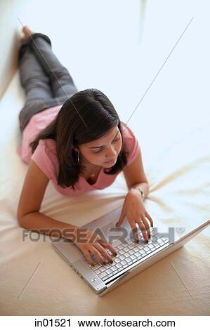 Stock Image - Woman at home, lying on bed, using laptop. Fotosearch