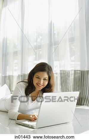 Stock Image - Woman at home, lying on floor, using laptop. Fotosearch