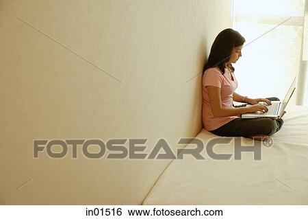 Stock Photograph - Woman at home, sitting on bed, using laptop. Fotosearch