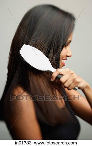 Stock Image - Woman brushing her hair, side view. Fotosearch