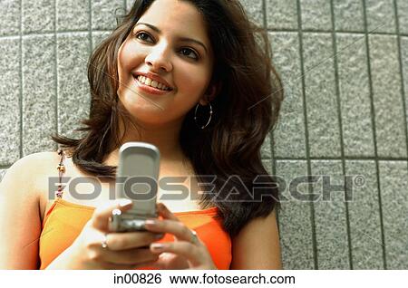 Woman holding mobile phone, smiling, looking away View Large Photo Image Stock Photograph - Woman holding mobile phone, smiling, looking away. Fotosearch