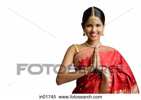 Stock Photography - Woman in red sari, standing with hands together, smiling at camera. Fotosearch