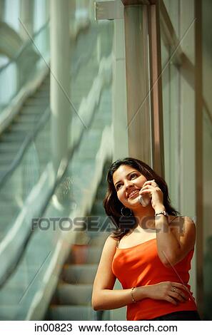 Stock Image - Woman leaning in glass wall using mobile phone, smiling. Fotosearch