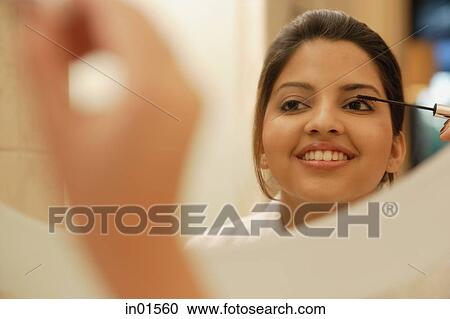 Stock Image - Woman looking in mirror applying mascara. Fotosearch