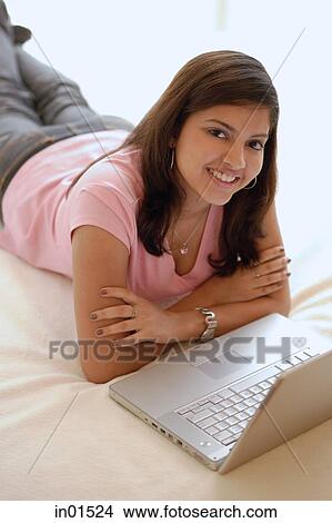 Picture - Woman lying on bed, arms crossed, laptop open in front of her, smiling. Fotosearch