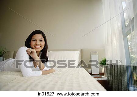 Stock Photo - Woman lying on bed smiling at camera. Fotosearch