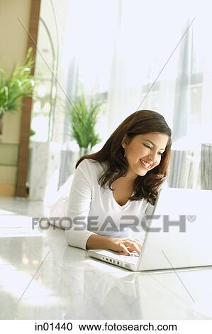 Stock Image - Woman lying on floor, using laptop, smiling. Fotosearch