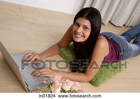 Picture - Woman lying on floor with laptop, smiling at camera. Fotosearch
