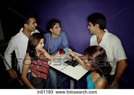 Stock Image - Young adults in club, toasting with drinks. Fotosearch