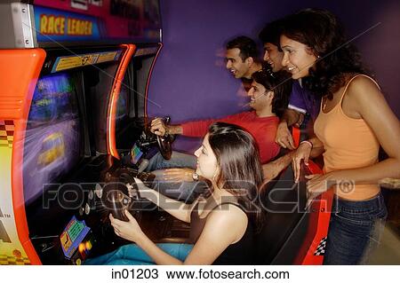 Stock Image - Young adults playing games in amusement arcade. Fotosearch