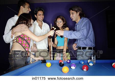 Stock Photography - Young adults standing around pool table, toasting with beer bottles. Fotosearch
