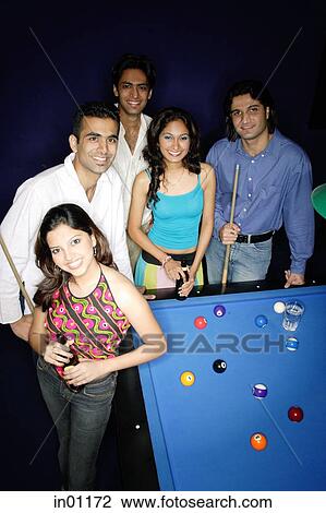Stock Image - Young adults standing around pool table. Fotosearch