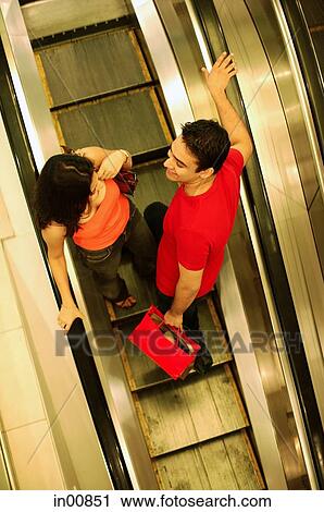 Young man and woman standing on escalator, high angle view View Large Photo Image Stock Image - Young man and woman standing on escalator, high angle view. Fotosearch