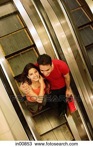 Young man and woman standing on escalator, woman looking up at camera View Large Photo Image Stock Image - Young man and woman standing on escalator, woman looking up at camera. Fotosearch