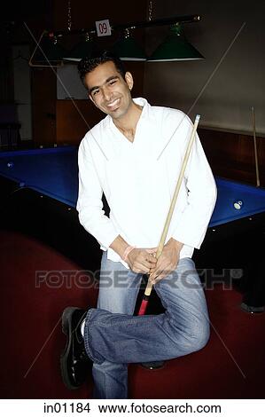 Young man leaning against pool table, holding pool cue View Large Photo Image Picture - Young man leaning against pool table, holding pool cue. Fotosearch
