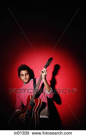 Young man playing guitar, standing against red background View Large Photo Image Stock Photography - Young man playing guitar, standing against red background. Fotosearch