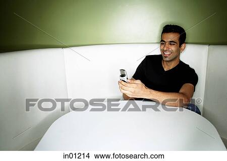 Picture - Young man sitting in booth, looking at mobile phone. Fotosearch
