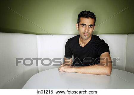 Stock Photography - Young man sitting in booth, looking at camera. Fotosearch