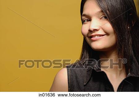 Stock Photograph - Young woman against yellow background, looking at camera, portrait. Fotosearch