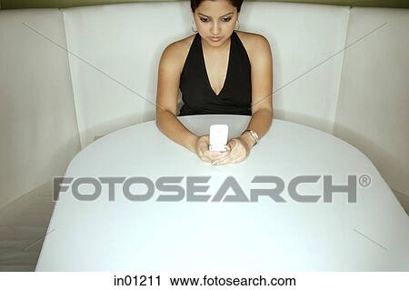 Young woman sitting in booth holding mobile phone View Large Photo Image Stock Image - Young woman sitting in booth holding mobile phone. Fotosearch