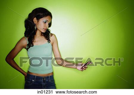 Young woman standing against green wall, looking at mobile phone View Large Photo Image Stock Image - Young woman standing against green wall, looking at mobile phone. Fotosearch