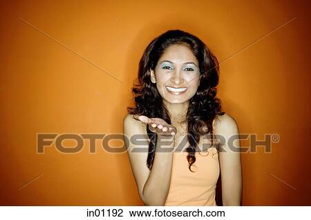Stock Image - Young woman standing against orange background, smiling at camera. Fotosearch