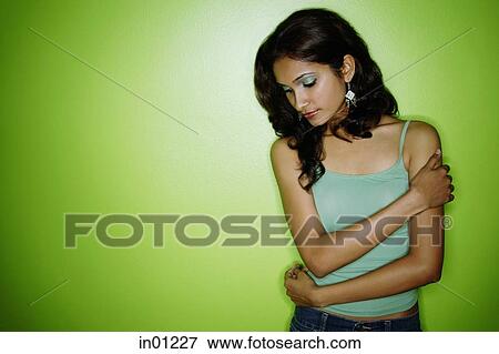 Stock Photo - Young woman tank top, arms around herself, looking down. Fotosearch
