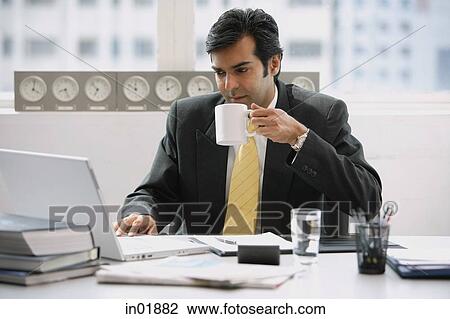 Businessman in office using laptop, drinking from cup View Large Photo Image Stock Image - Businessman in office using laptop, drinking from cup. Fotosearch