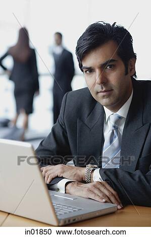 Businessman sitting in front of laptop, looking at camera View Large Photo Image Stock Image - Businessman sitting in front of laptop, looking at camera. Fotosearch