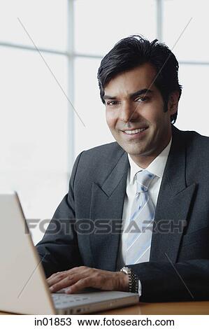 Businessman sitting in front of laptop, looking at camera View Large Photo Image Stock Image - Businessman sitting in front of laptop, looking at camera. Fotosearch