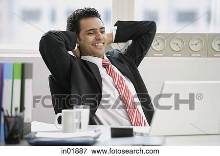 Businessman sitting in office, hands behind head, smiling View Large Photo Image Stock Photo - Businessman sitting in office, hands behind head, smiling. Fotosearch