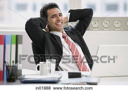 Businessman sitting in office, hands behind head, smiling at camera View Large Photo Image Stock Photo - Businessman sitting in office, hands behind head, smiling at camera. Fotosearch