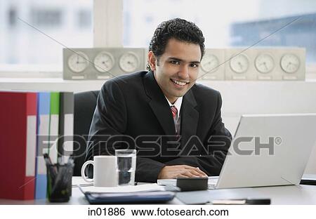 Businessman sitting in office, smiling at camera View Large Photo Image Stock Photograph - Businessman sitting in office, smiling at camera. Fotosearch