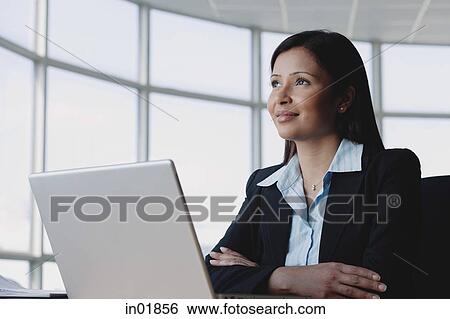 Businesswoman sitting in front of laptop, arms crossed, looking away View Large Photo Image Stock Photograph - Businesswoman sitting in front of laptop, arms crossed, looking away. Fotosearch