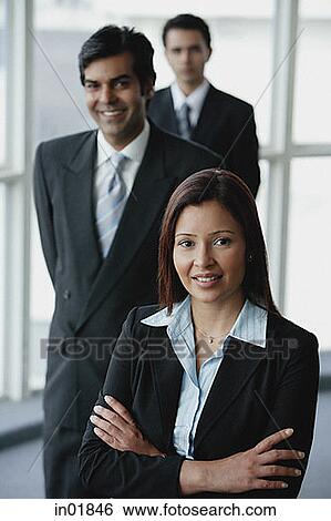 Stock Photograph - Businesswoman smiling at camera, businessmen behind her. Fotosearch