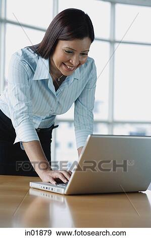 Businesswoman using laptop, leaning on table View Large Photo Image Stock Photo - Businesswoman using laptop, leaning on table. Fotosearch