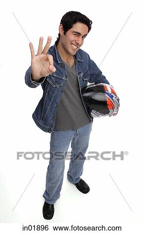 Man carrying motorcycle helmet, looking up at camera, making hand sign View Large Photo Image Stock Photograph - Man carrying motorcycle helmet, looking up at camera, making hand sign. Fotosearch