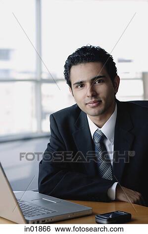 Young businessman next to laptop, looking at camera View Large Photo Image Stock Photograph - Young businessman next to laptop, looking at camera. Fotosearch