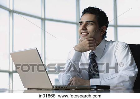 Young businessman sitting in front of laptop, smiling, looking away View Large Photo Image Stock Photo - Young businessman sitting in front of laptop, smiling, looking away. Fotosearch