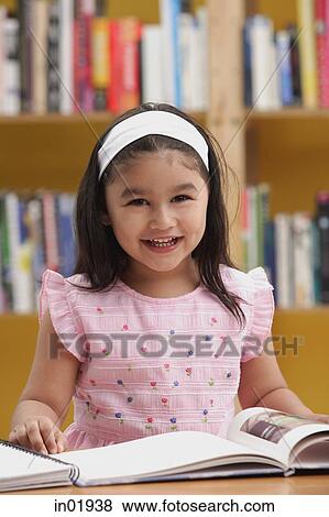 Stock Photo - Young girl reading a book, smiling at camera. Fotosearch
