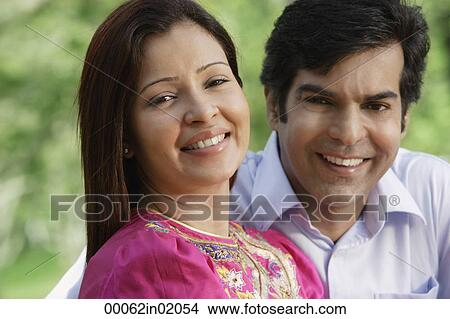 A couple smile at the camera as they sit together in the park View Large Photo Image Picture - A couple smile at the camera as they sit together in the park. Fotosearch