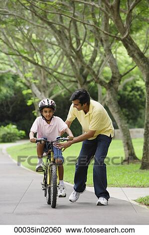 Stock Image - A father teaches his son to ride a bike. Fotosearch