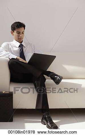 A man sits on a couch with a laptop View Large Photo Image Stock Photo - A man sits on a couch with a laptop. Fotosearch