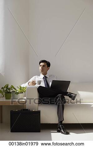 A man sits on a couch with a laptop View Large Photo Image Stock Photo - A man sits on a couch with a laptop. Fotosearch