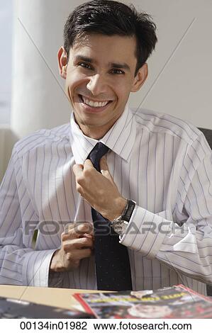 Stock Image - A man smiles as he adjusts his tie. Fotosearch