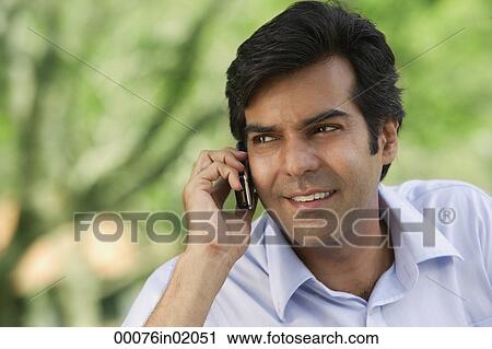 Stock Image - A man talks on his cellphone in the park. Fotosearch