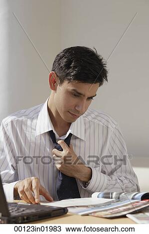 Stock Image - A man works at a desk as he loosens his tie. Fotosearch