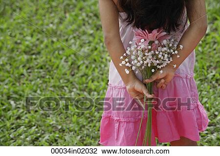 A small girl holds flowers behind her back View Large Photo Image Stock Image - A small girl holds flowers behind her back. Fotosearch