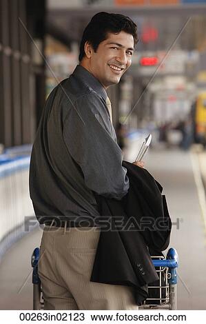 Stock Image - Man pushing trolley in airport, smiling at camera. Fotosearch