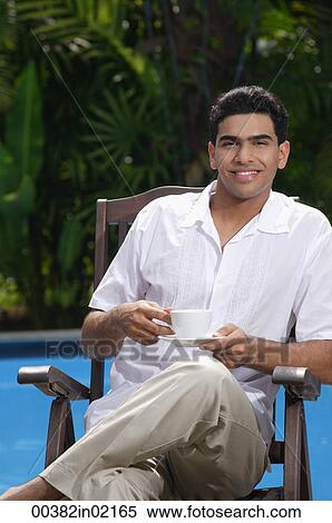 Man sitting in chair by the pool, holding a cup and looking at camera View Large Photo Image Stock Photography - Man sitting in chair by the pool, holding a cup and looking at camera. Fotosearch